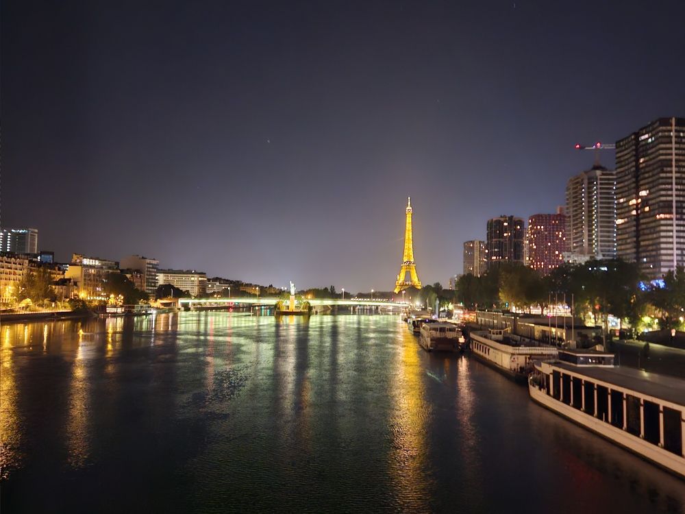 The Eiffel tower is seen in the dark. The light reflects from the Seine.