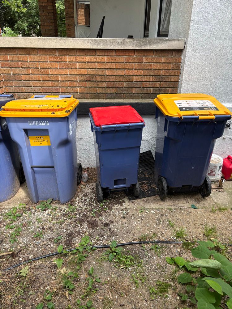 The smallest sized trash can next to the two large recycling bins.