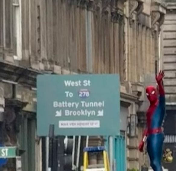Slightly blurry photo of Spider-man waving, next to a sign that says “Weat street to Battery Tunnel and Brooklyn”