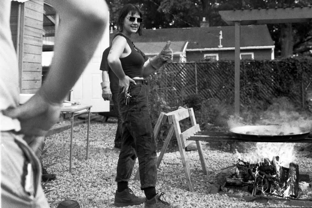 a film photo of a person giving a thumbs up in a welding glove next to a large fire and a paella pan