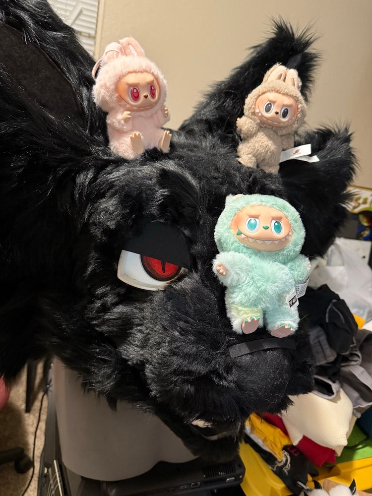 A photo of a finished fursuit head of a black cat with red eyes and labubus on his head 