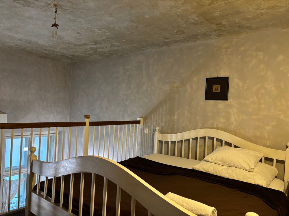 A bedroom with a balcony overlooking the living room. The bed is worryingly close to the ceiling. The paintwork is amazingly splotchy 