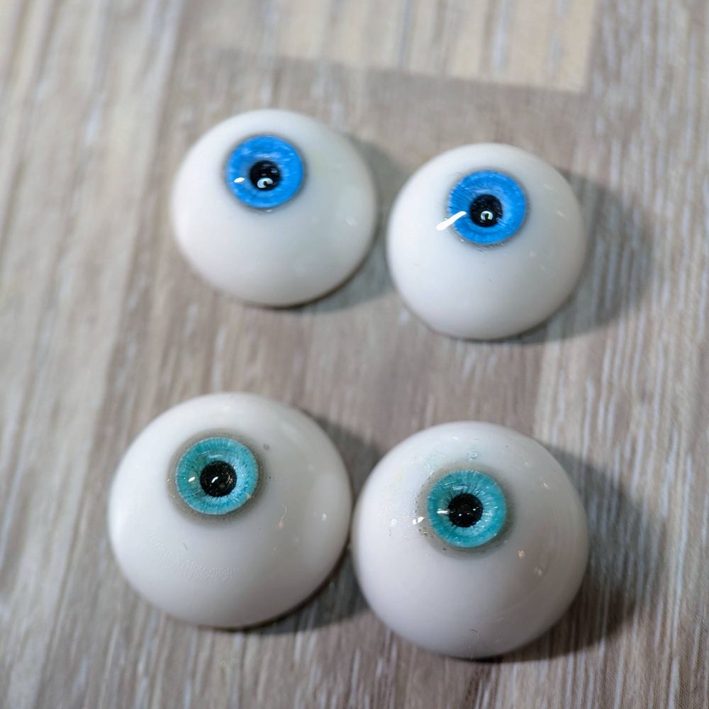 a pair of blue resin doll eyes next to larger pair of blue-green resin doll eyes