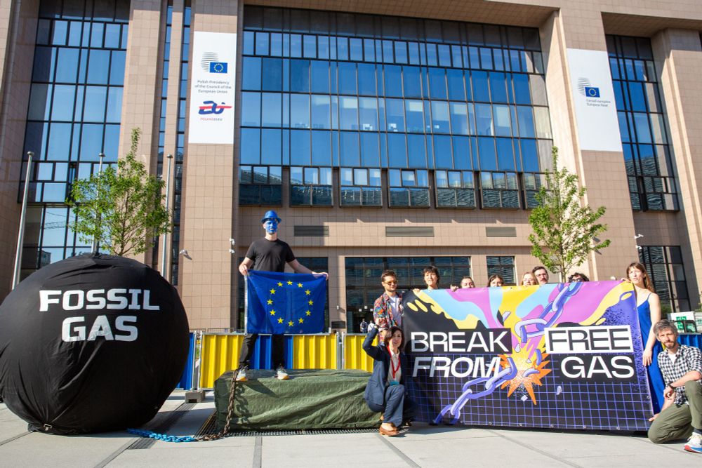 A group of people in front of a colourful banner that says Break Free from Fossil Gas next to a person dressed as the EU chained to a big prisoner’s ball that says fossil gas 