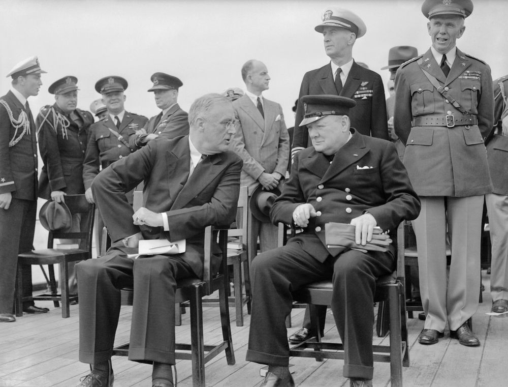 President Roosevelt and Winston Churchill (in uniform) seated on the quarterdeck of HMS Prince of Wales for a Sunday service during the Atlantic Conference, 10 August 1941. Credit: Royal Navy photographer 