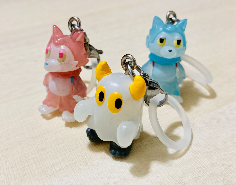 ガシャポンの「おおかみくんとなかま めじるしアクセサリー」のマスコット3つ。
手前に白い布地に角が生えたニセおばけ、左奥に赤いおおかみくん、右奥に青いおおかみくんがいる。