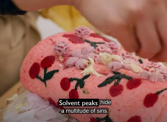 A close up of an intricately decorated swiss roll with frosting over a noticeable crack.  Superimposed is the text "Solvent peaks hide a multitude of sins"