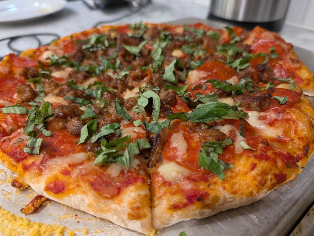 Photo of a pizza freshly baked with pepperoni, sausage, and torn shreds of basil on top.
