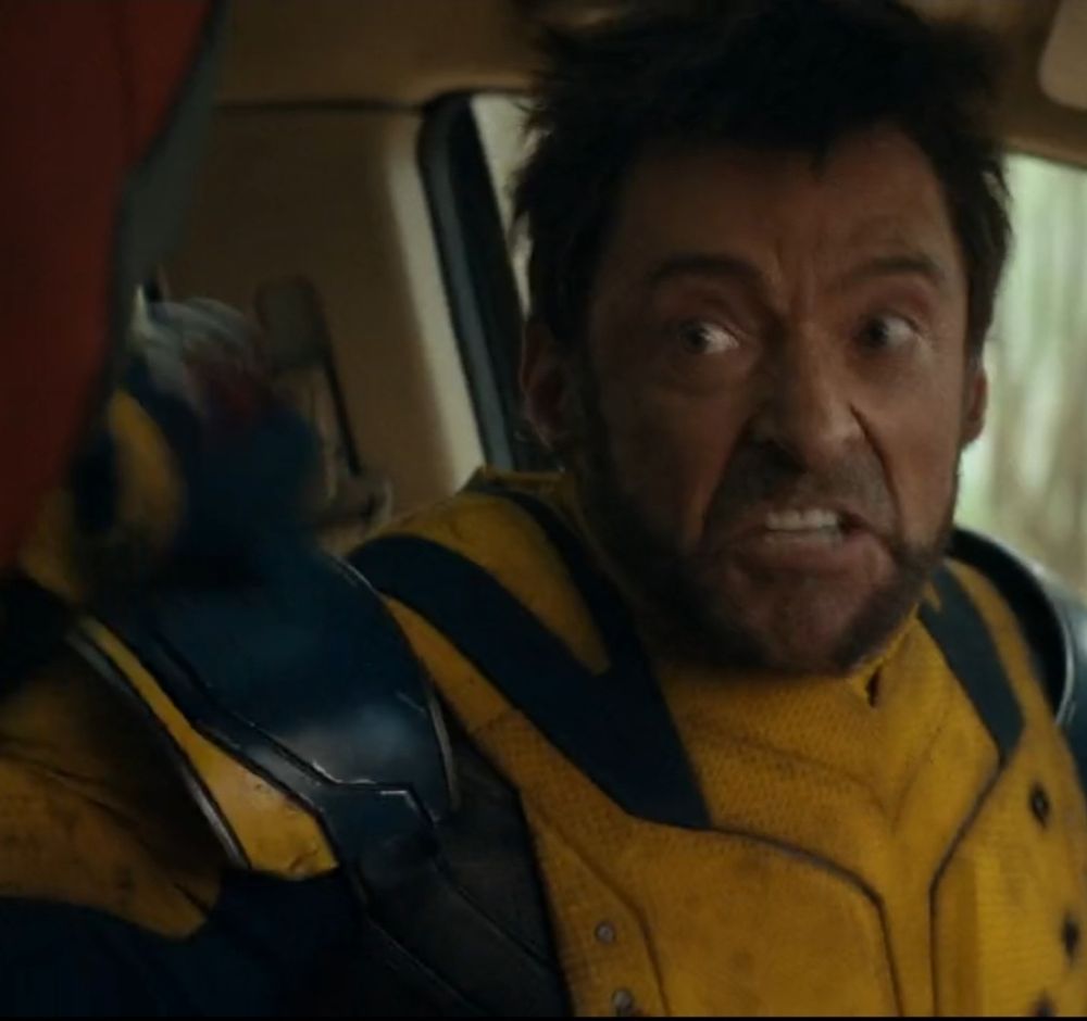Hugh Jackman as Wolverine in the driver's seat of a vehicle lunging at the passenger in a fit of rage. 