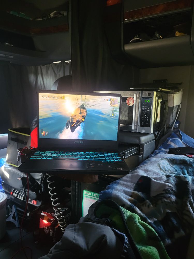 A computer sits next to a bed in front of a microwave inside a semi truck with velheim displayed on the screen