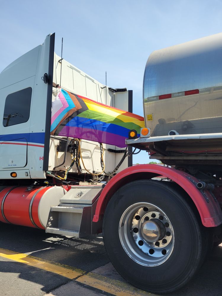 An inclusive pride flag flies behind the cab of a semi truck. 