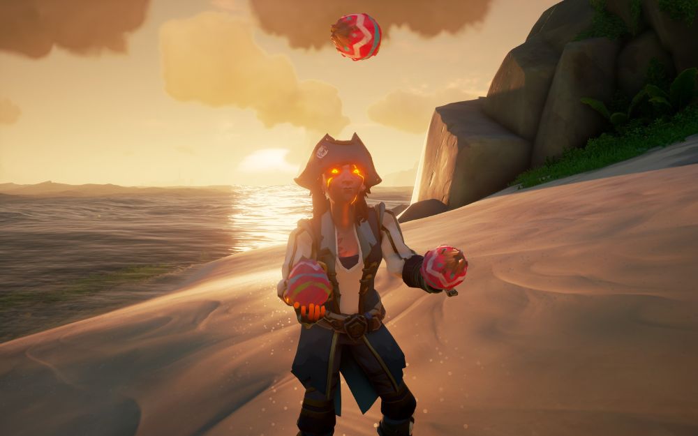 A pirate with fiery red eyes juggles three painted coconuts on the shore while the sun sets behind her.