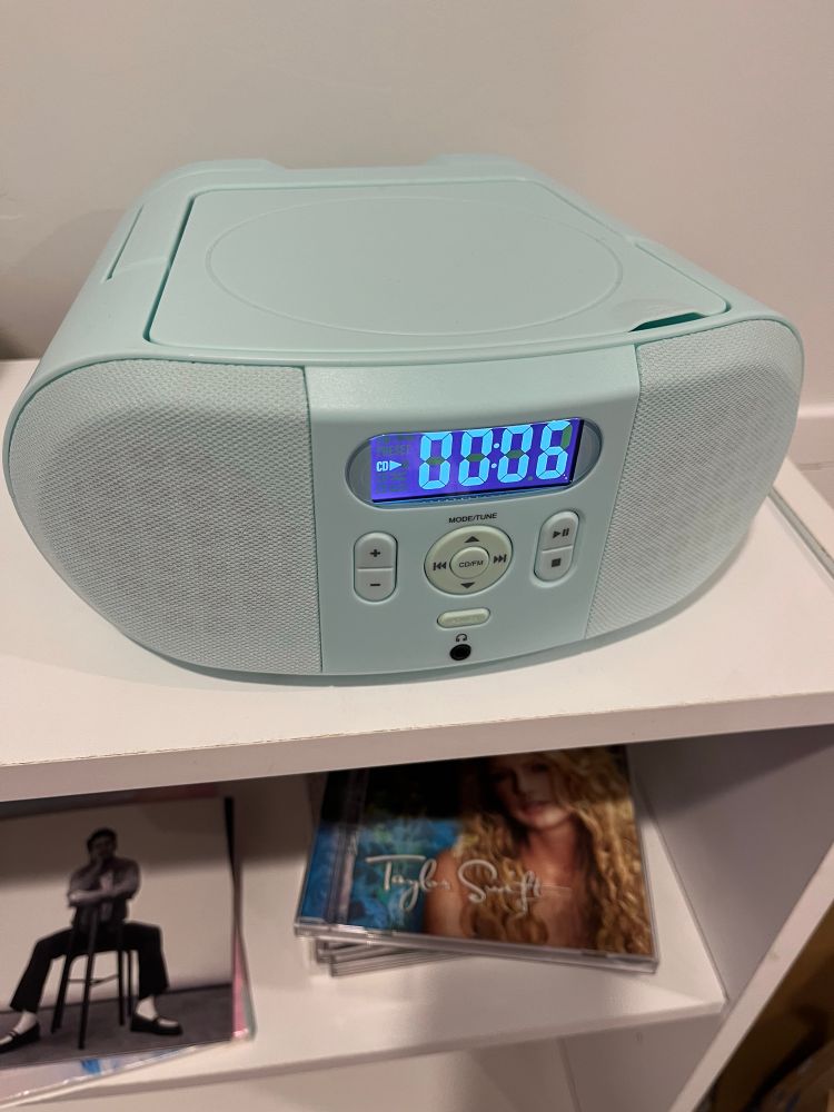 A cd player sitting on a bookshelf with a pile of CDs nearby