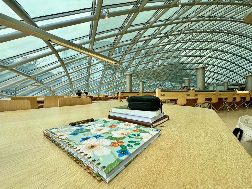 Photo of journals and books placed on a desk with glass ceiling views taken at The Joe and Rika Mansueto Library 