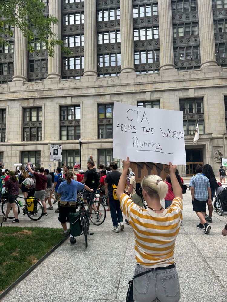 A crowd of attendees marching the street with a person holding a sign that says “CTA keeps the world running” 