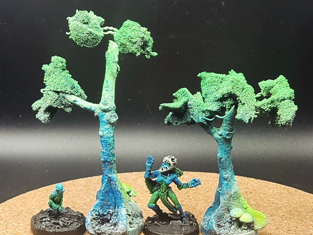 Photographs of handpainted miniatures: a monkey, a mesoamerican woman, and two scratchbuilt trees. All airbrushed neon blue and green.