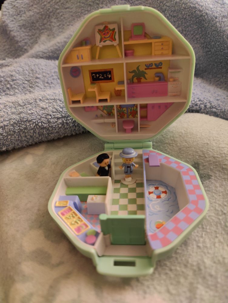 Dieselbe Schatulle geöffnet; es zeigen sich verschiedene Schulräume. Vor einer Treppe steht Polly in veilchenblauer Schuluniform, neben ihr ein in schwarz gekleideter Herr, wahrscheinlich der Direktor.