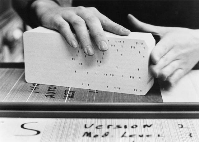 Black and white photo of a pair of hands holding a stack of computer punch cards.