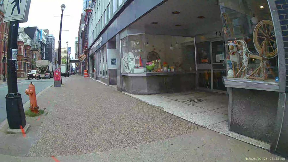 A screenshot from a video showing an 18-wheel grain truck swerving into oncoming traffic on a narrow, two-lane downtown street to get around an illegally parked cube van