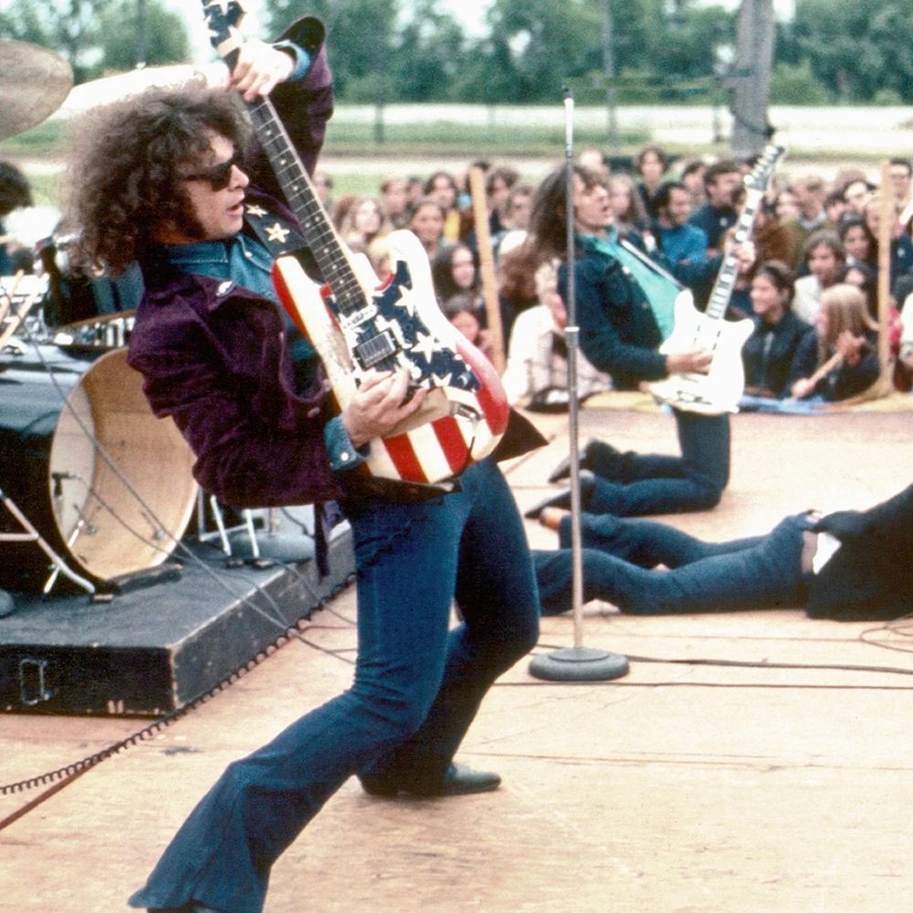 Wayne Kramer arcs his back playing a guitar painted to look like an American flag. 