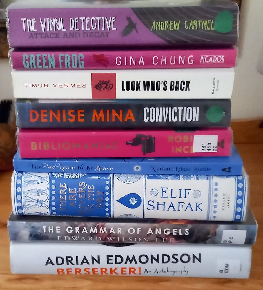 A pile of books: Berserker by Adrian Edmondson, Bibliomaniac by Robin Ince, How we learn to be brave by Mariann Edgar Budde, There are rivers in the sky by Elif Shafak, Green Frog by Gina Chung, Look Who’s Back by Timur Vermes, Attack and Decay by Andrew Cartmel, Conviction by Denise Mina, The grammar of angels by Edward Wilson-Lee.