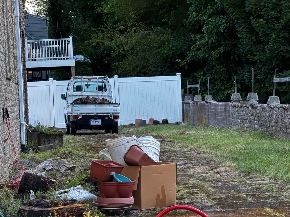 In this picture, you see a brick building to the left, a brick wall to the right a road surrounded by grass, some junk right up front that’s going to be thrown out the next day, and in the distance right before a wall is my Japanese Subaru truck Loaded up and ready to go to the dumps tomorrow
