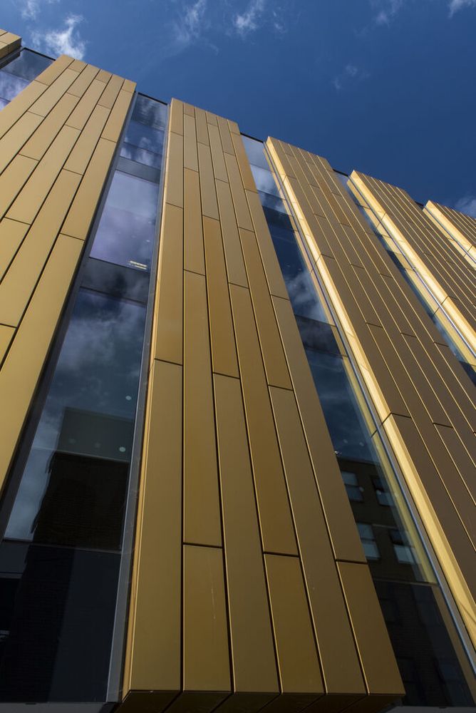 Looking up a gold and glass building toward a blue sky with a few scattered clouds. 

