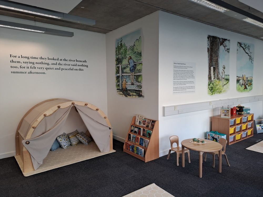 Room with child's tent with cushions, a small child's bookcase, a small table with two chairs, a chest with grey and yellow plastic drawers, and art and text on the walls from Winnie the Pooh - Christopher Robin and Pooh looking over the bridge at the river, and Christopher Robin by a tree
