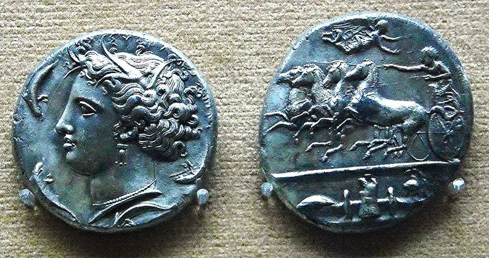 Image: Coin of Syracuse of Dionysius I: 405-367 BCE (Obverse) with the head of the Nymph Arethusa between the dolphins; Quadriga and weapons (Reverse) – Naples, Archaeological Museum. Courtesy of Carlo Raso on Flickr.