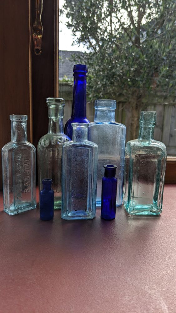 Several blue glass bottles of various shapes and sizes on a counter in front of a window 