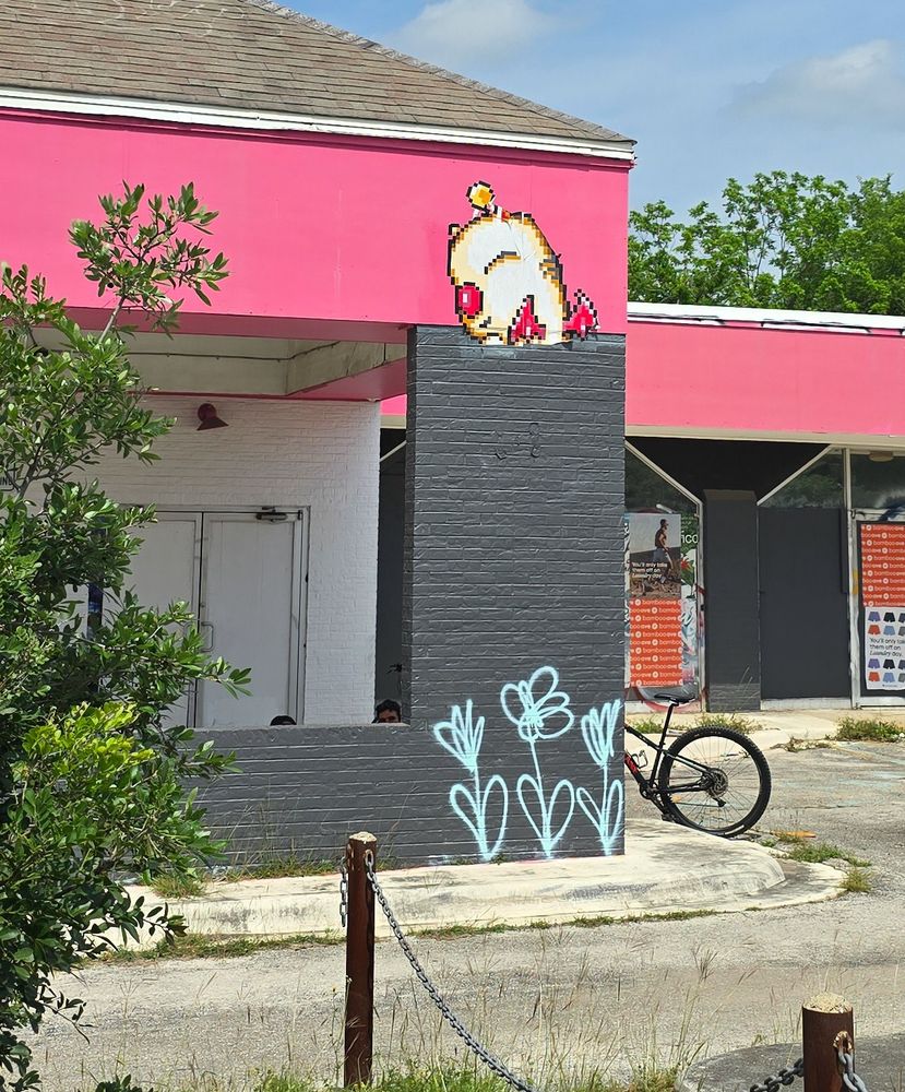 A #wheatpaste on a building of a pixelated Moogle, Final Fantasy 3 style. There are also white spray painted flowers. 