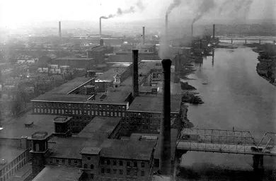 Black and white photo of smoke stacks of Lowell beside the river. Source: https://www.nps.gov/media/photo/gallery-item.htm?id=393f4e51-fe8f-41b0-9776-fdfa8efdea78&gid=06FA0E8B-9F13-491D-A47C-6AE71373E232
