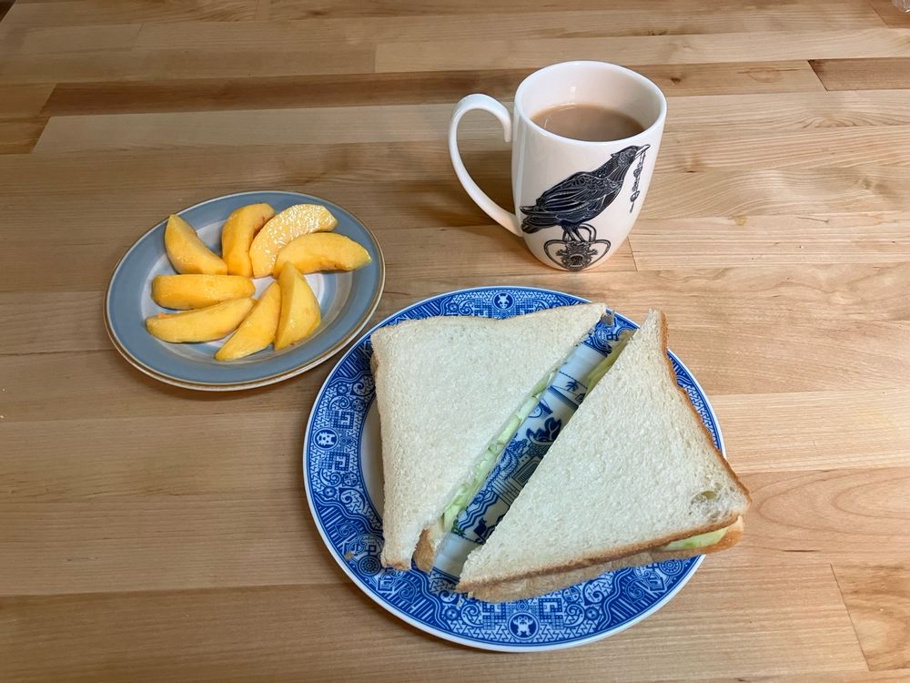 A cup of tea, a sandwich, and a cut up peach. 