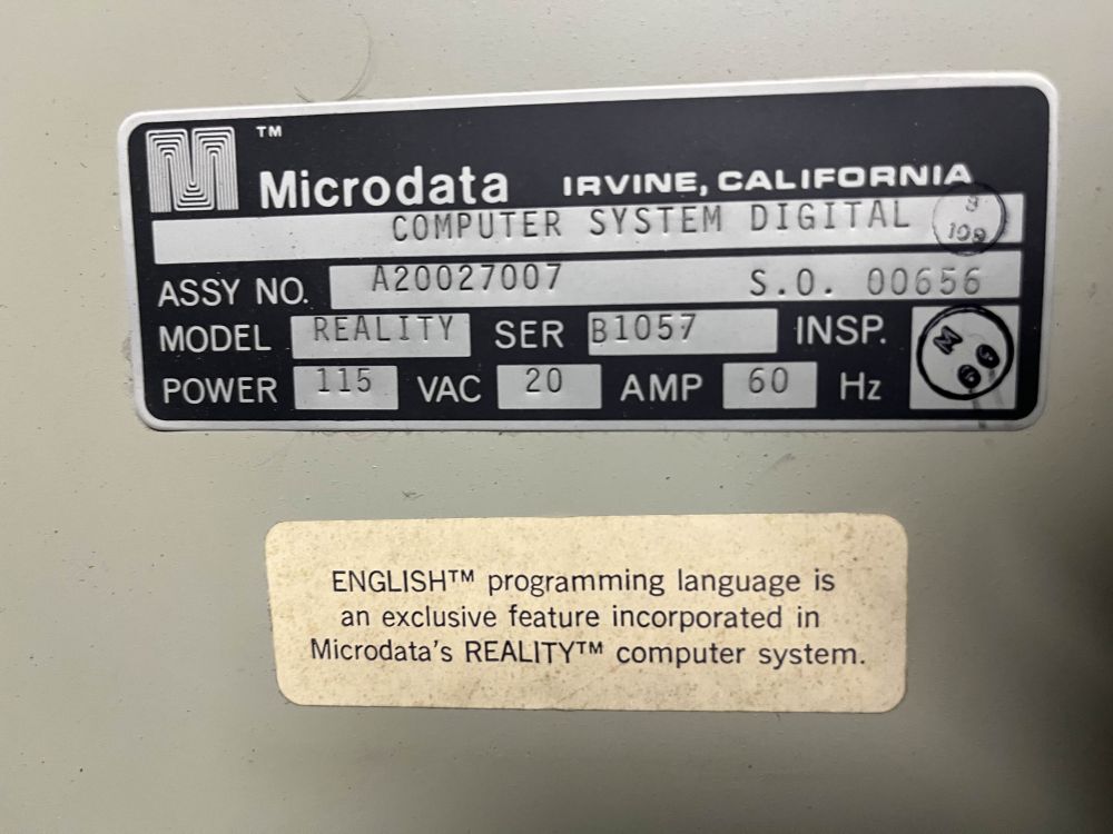 A photo of a Microdata model plate for a mid-70s REALITY system, below which a sticker reads "ENGLISH(TM) programming language is an exclusive feature incorporated in Microdata's REALITY(TM) computer system.