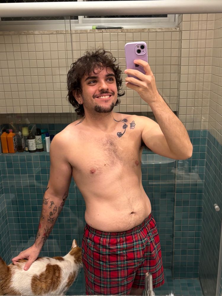 Homem sem camisa de samba canção acaricia gato alaranjado