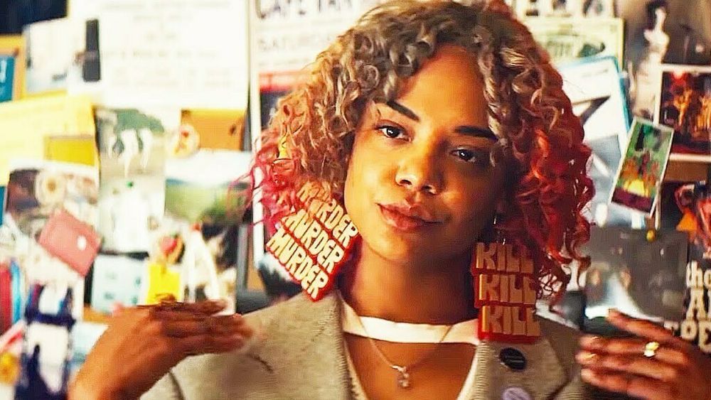 Tessa Thompson in SORRY TO BOTHER YOU, with blonde curly hair and a “idgaf” look on her face, wearing a pair of earrings in big, gold lettering that read “MURDER MURDER MURDER” or “KILL KILL KILL”