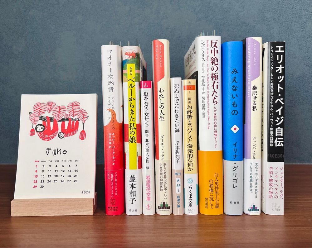 10冊の本が棚の上に背表紙を向けて並んでいる。本の列の左側には、6月の卓上カレンダー（ナマケモノの親子のイラスト）が置かれている。本のタイトルは左から順に、
◆『マイナーな感情　アジア系アメリカ人のアイデンティティ』キャシー・パーク・ホン／池田年穂 訳（慶應義塾大学出版会）
◆『ペルーからきた私の娘』藤本和子（晶文社）
◆『塩を食う女たち　聞書・北米の黒人女性』藤本和子（岩波現代文庫）
◆『私の人生』ダーチャ・マライーニ／望月紀子 訳（新潮クレスト・ブックス）
◆『死ぬまでに行きたい海』岸本佐知子（新潮文庫）
◆『増補版・お砂糖とスパイスと爆発的な何か』北村紗衣（ちくま文庫）
◆『反中絶の極右たち　なぜ女性の自由に恐怖するのか』シャン・ノリス／牟礼晶子訳（明石書店）
◆『みえないもの』イリナ グリゴレ（柏書房）
◆『翻訳する私』ジュンパ・ラヒリ／小川高義訳（新潮クレスト・ブックス）
◆『Pageboy  エリオット・ペイジ自伝』エリオット・ペイジ／長尾莉紗訳（DU BOOKS）
