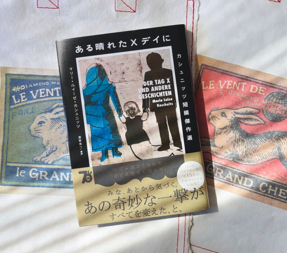 洋風レトロな兎の絵がプリントされた袋の上に『ある晴れたXデイに』が置かれている写真。本の帯には、「みな、あとから気づく。あの奇妙な一撃がすべてを変えた、と。」と書かれている。