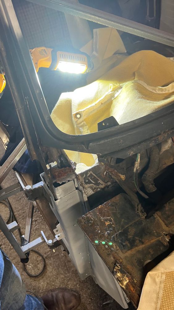A close up of a car in a workshop showing the area around the base of the windscreen and top of the front wing. Large areas of bodywork have been removed, and some further rust is visible. Other parts are new and painted with primer.