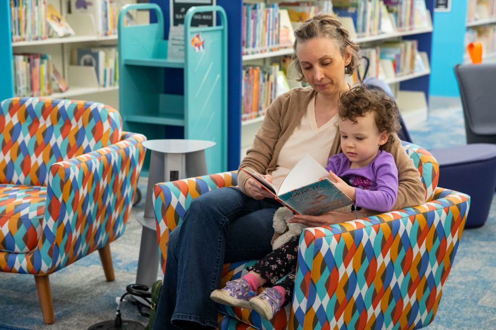 Mother and daughter sit in a brightly colored chair reading a picture book.