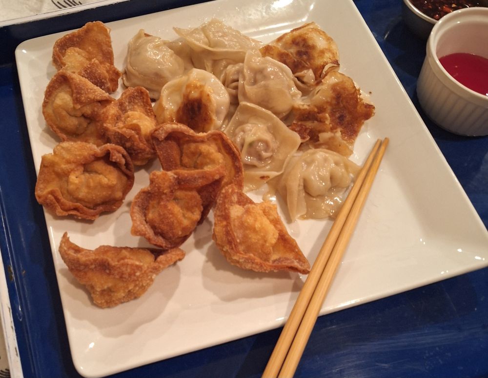 A photo of a square plate of wontons on a blue tray. Half are deep fried and half are pan fried. Little ramekins of Cherry sauce and chili crisp can be seen in the upper right corner next to the plate. Chopsticks also sit on the plate.