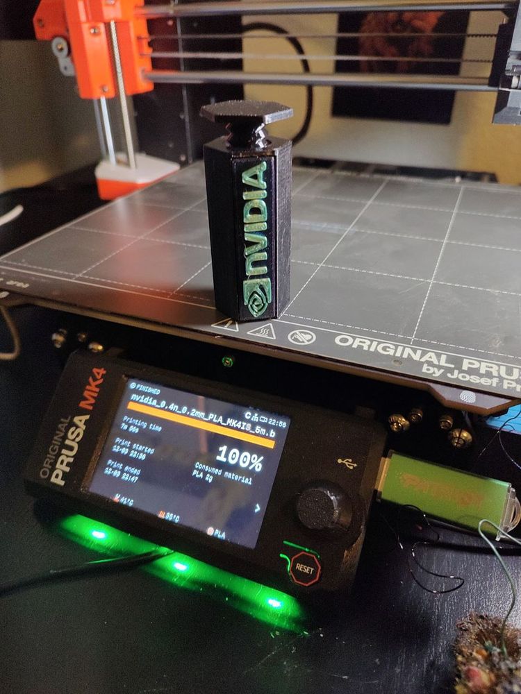 Picture of a 3d-printed gpu-support - it's a black hexagon shaped cylinder with a tapped hole allowing a threaded screw with a flat top to descend snugly or rise to provide GPU support.  nvidia branded in green. Cylinder measures appx 67mm when closed.