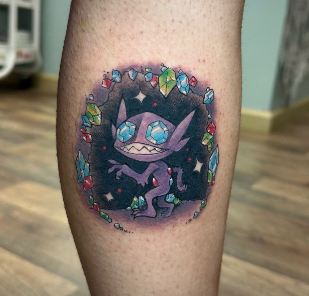 A tattoo on a person's leg of the Pokemon Sableye in a gem cave