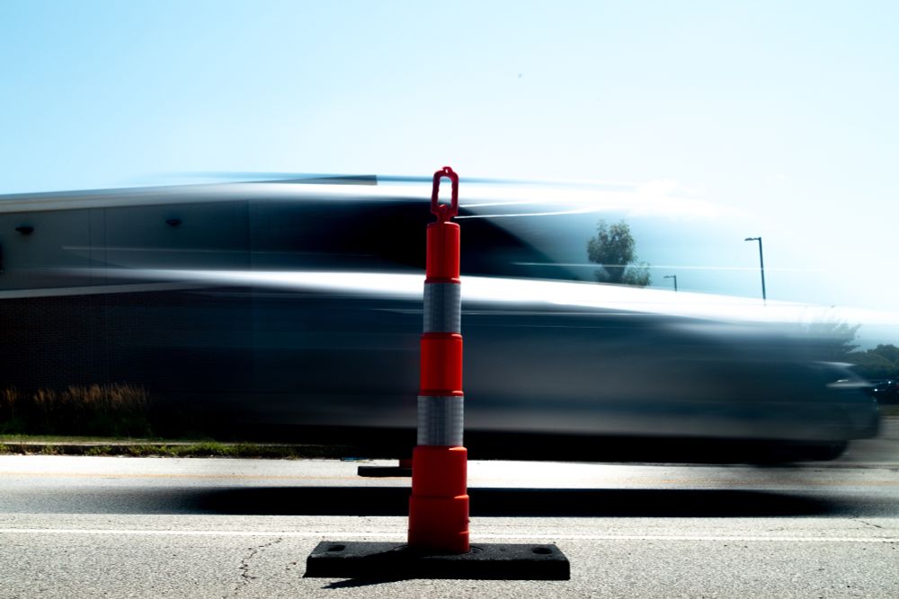 A car blurs past a pair of large reflective orange and white traffic cones. 