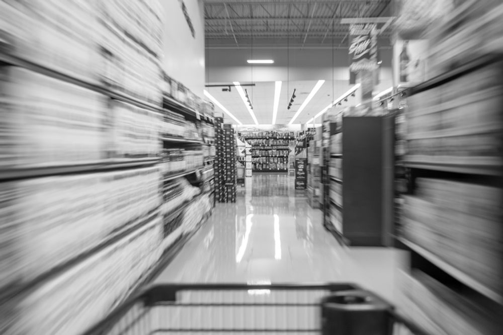 A grocery store cart moves down the aisle of a grocery store. 