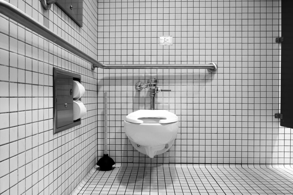 A photo looking head on at a handicap assessable toilet in a public bathroom.  