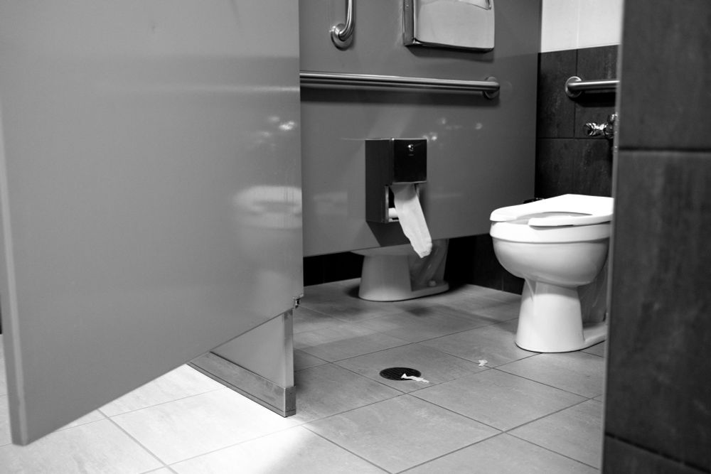 A black and white photo of a dirty bathroom stall. 