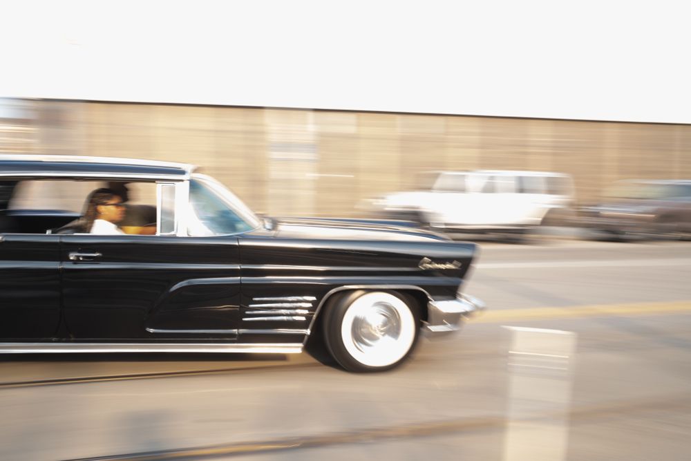 A black and chrome 1960’s era Lincoln Continental appears to speed down the street. 