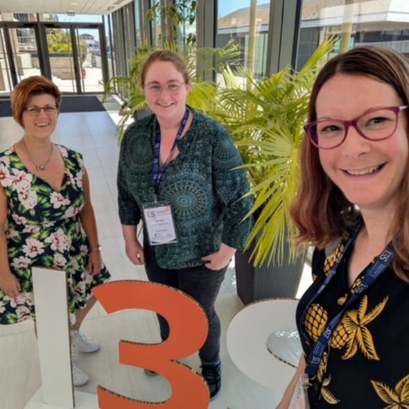Emma Water (L), Alice Nisbet (M) and Gemma Langridge (R) attend the International Symposium on Salmonella & Salmonellosis, standing in front of a sign that reads 'I3S' for the conference.