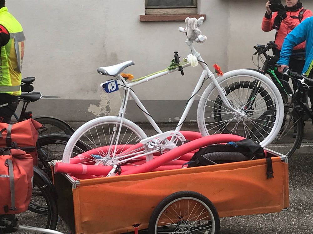 Ein weißes Rad ist auf einem Fahrradanhänger befestigt. Im Anhänger liegen rote Pool-Nudeln.